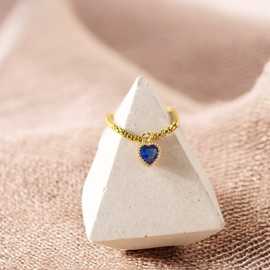 image shows a gold birthstone heart ring on a display cone on a neutral background