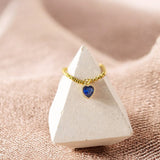 image shows a gold birthstone heart ring on a display cone on a neutral background