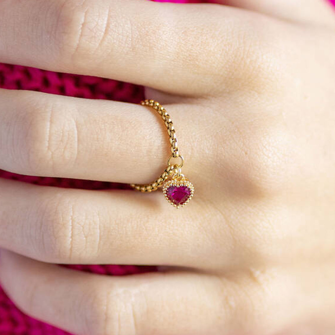 image shows a hand wearing a gold heart birthstone ring with July birthstone