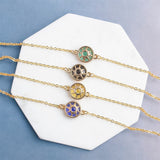 Image shows four coloured glass sun symbol bracelets in gold lying onwhite hexagon marble slap on blue fabric