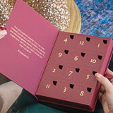 Image shows model opening the 12 Days of JOY Advent Calendar with the closed, numbered doors displayed. Text inside the calendar reads: 