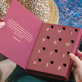 Image shows model opening the 12 Days of JOY Advent Calendar with the closed, numbered doors displayed. Text inside the calendar reads: 