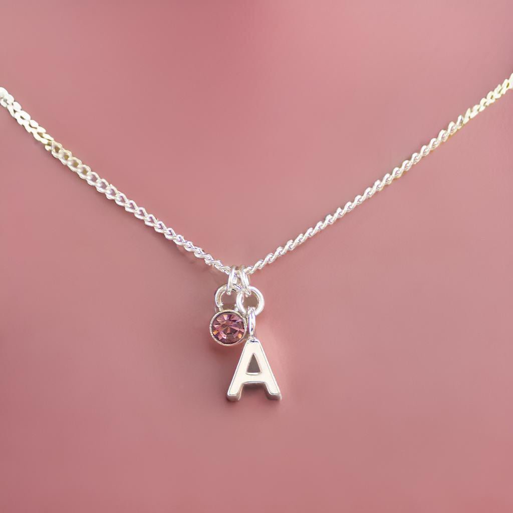 image shows a silver necklace with initial A and rose October birthstone charms on a plain pink background