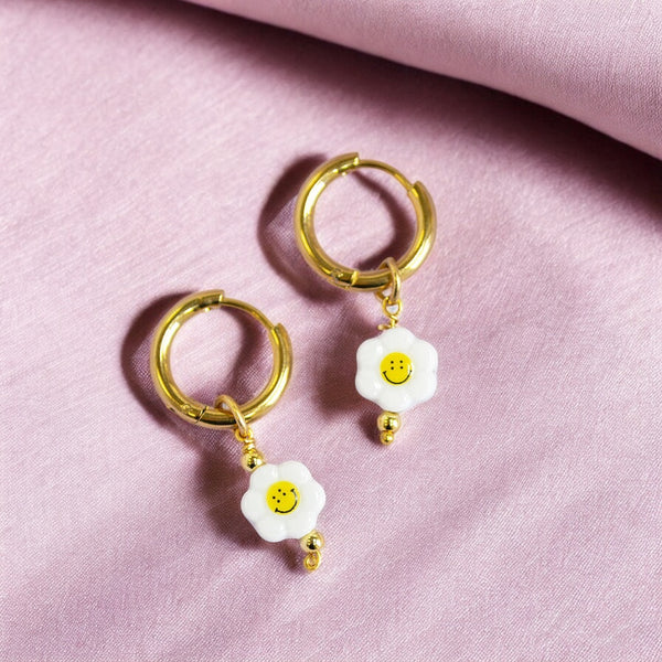 Image shows smiley face flower hoop earrings on a mauve fabric background