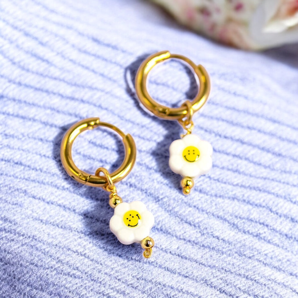 Image shows smiley face flower hoop earrings on a blue stripey fabric background