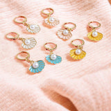 image shows colourful enamel shell earrings on a pale peach fabric background