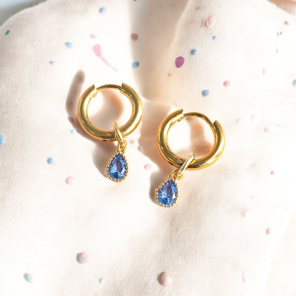 image shows a pair of gold plated hoop earrings with teardrop birthstone detail for December birthdays