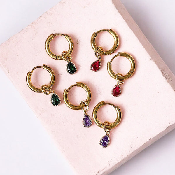 image shows a selecti0n of teardrop birthstone gold hoop earrings on a pink ceramic background