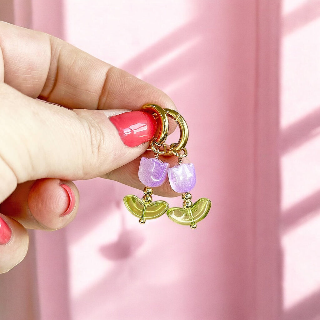 Image shows a woman'd hand holding upa pair of glass tulip hoop earrings in front of a pink wall with sun streaming in the window