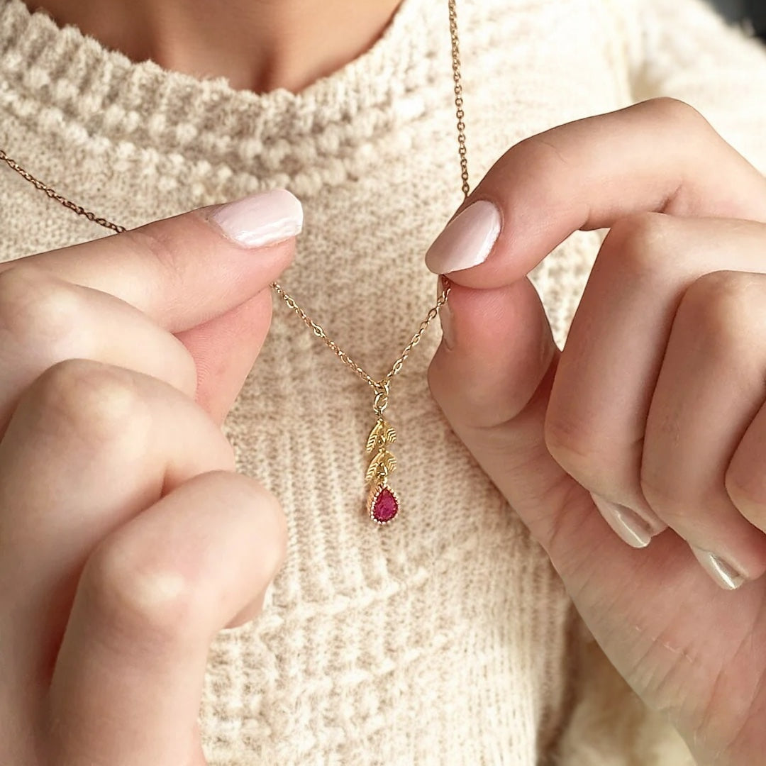 image shows woman in a cream jumper wearing a leaf chain necklace with July Ruby stone