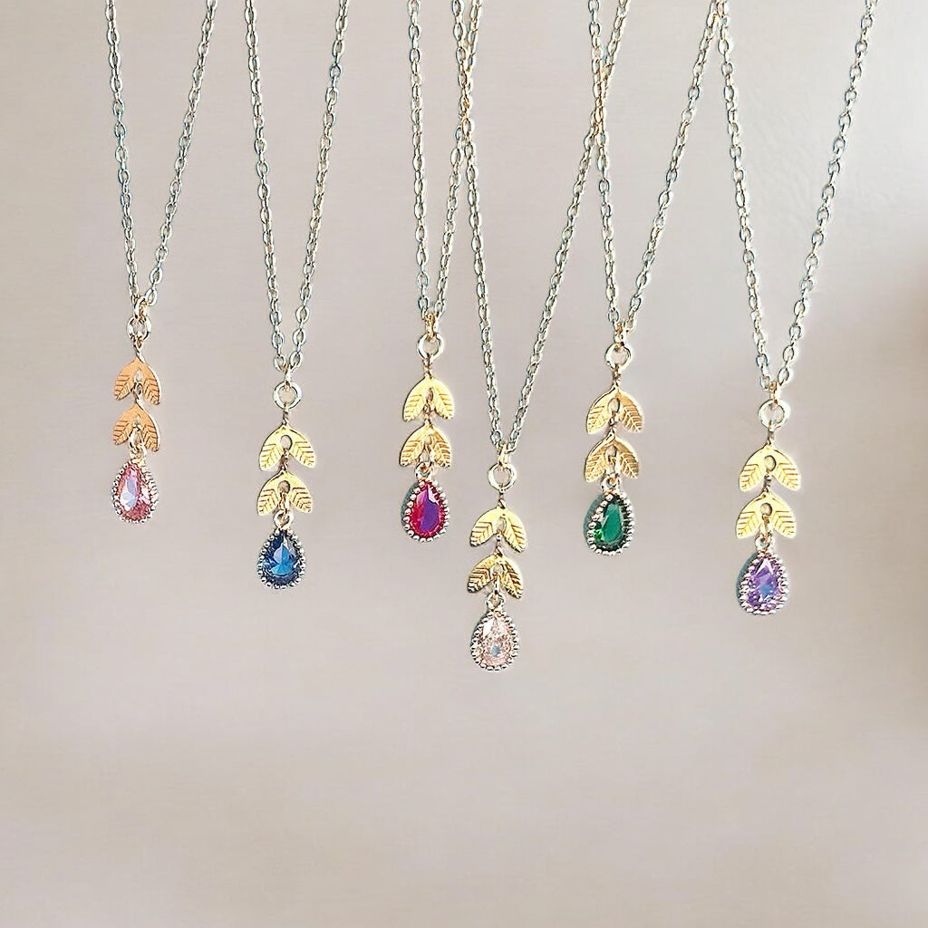 image shows a selection of gold leaf chain necklaces with birthstone detail against a neutral background