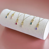 image shows a selection of gold leaf chain necklaces with birthstone detail on a velvet jewellery display tube