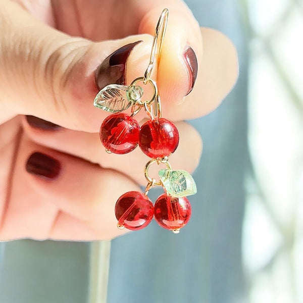 Image shows a hand holding up a pair of handmade gold plated glass cherry earrings