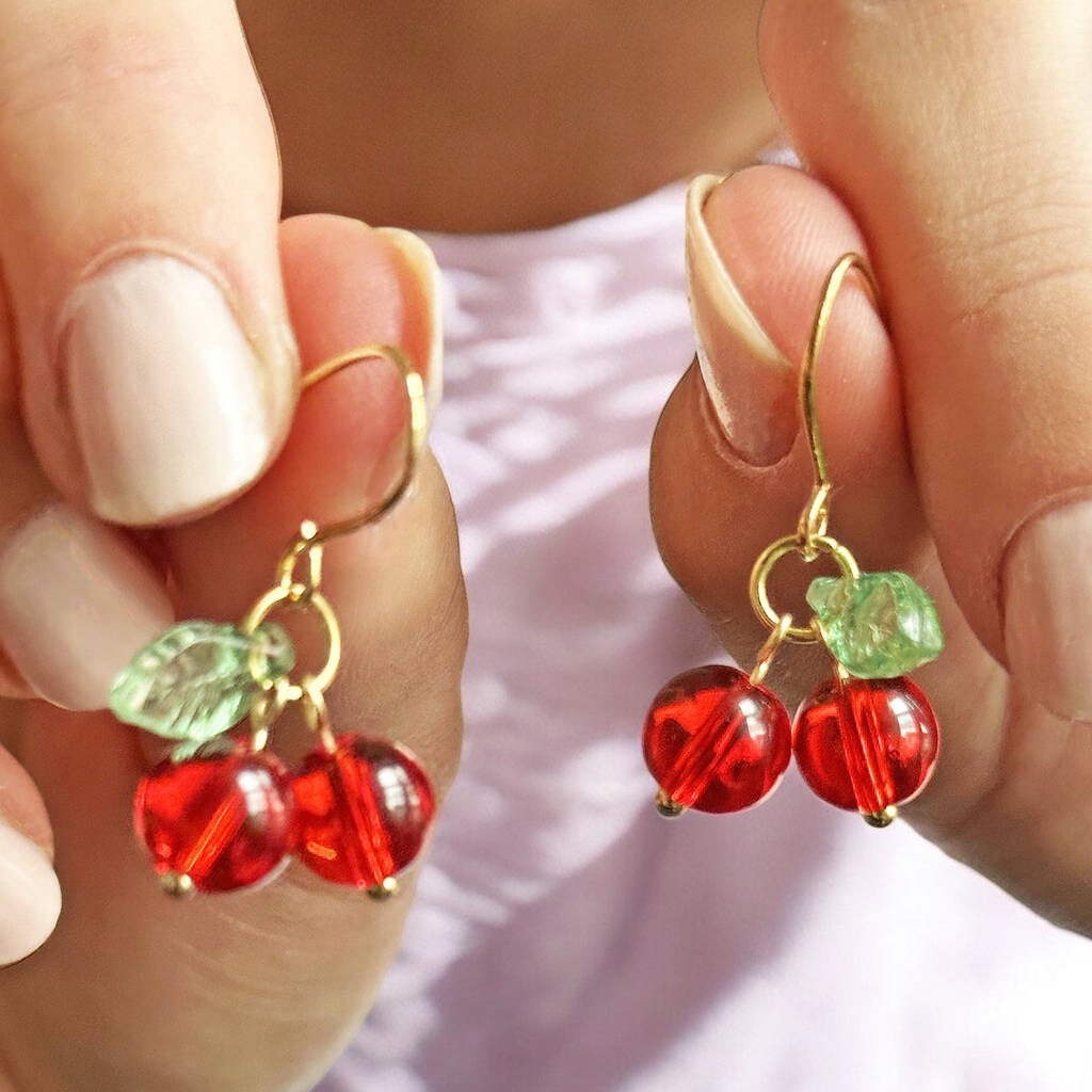 Image shows a hand holding up a pair of handmade gold plated glass cherry earrings