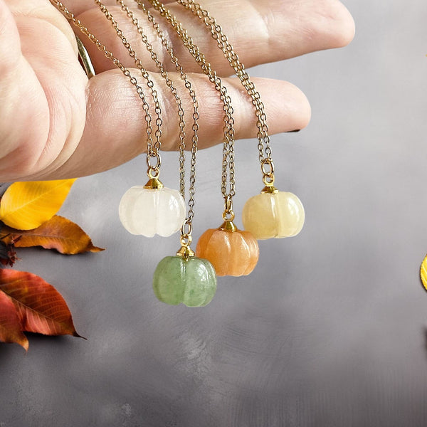 Image shows a woman's hand holding four pumpkin necklaces again a great background with autum leaves detail