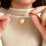 Image shows a woman in a beige jumper holding an orange pumpkin necklace that she is wearing round her neck.