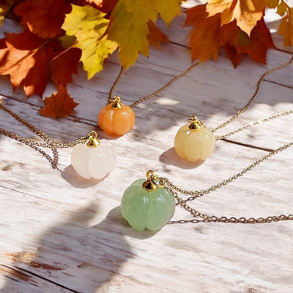 Image shows four gemstone pumpkin necklaces on a whitewashed wooden surface with autumn leaves in the background