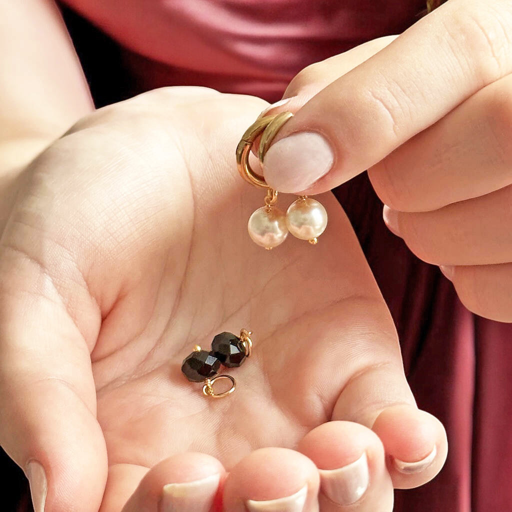 image shows hands holding mix and match day to night pearl and black crystal hoop earrings