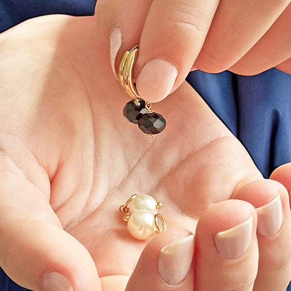 image shows hands holding mix and match day to night pearl and black crystal hoop earrings