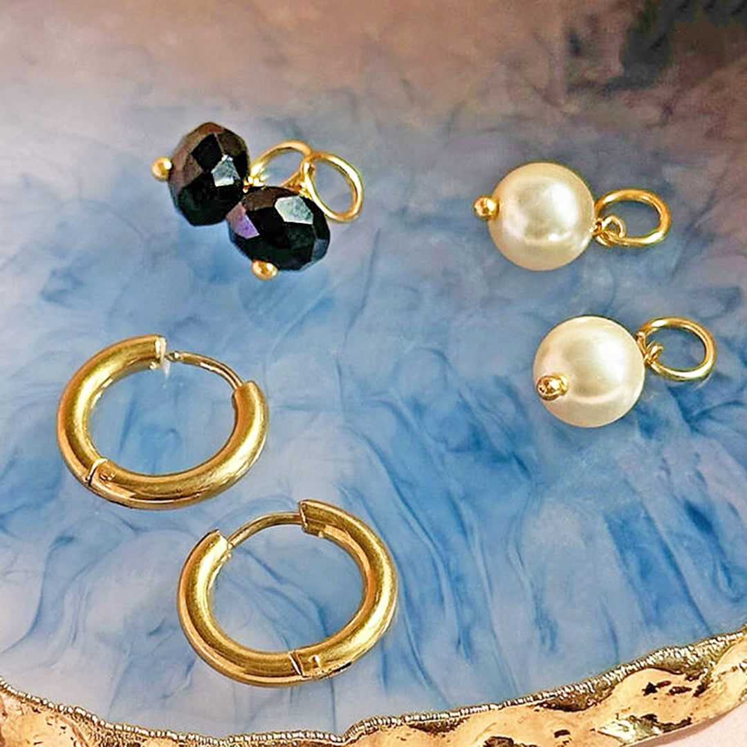 image shows gold hoop earrings with mix and match pearl and black crystal charms on a blue marbled surface