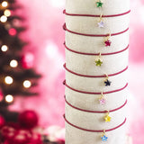 image shows a stack of maroon cord friendship bracelets with birthstone star charms in front of a pink festive backdrop