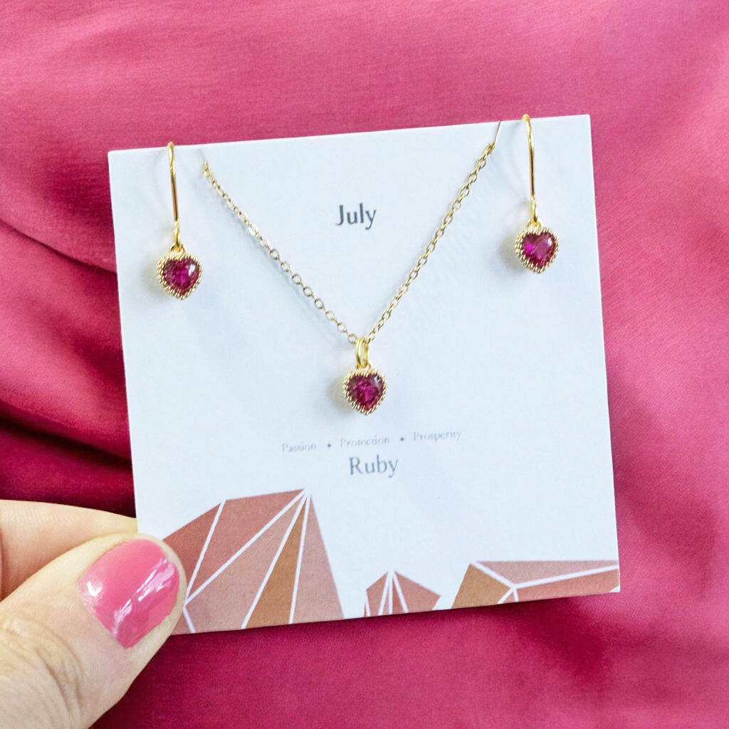 Image shows a birthstone jewellery set on a birthstone characteristics card on a bright pink background