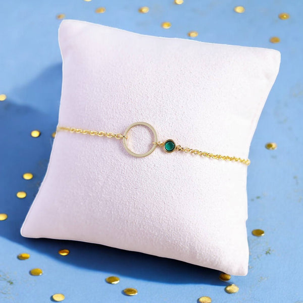 image shows a gold circle birthstone bracelet on a pink display cushion with a blue and gold dotted background