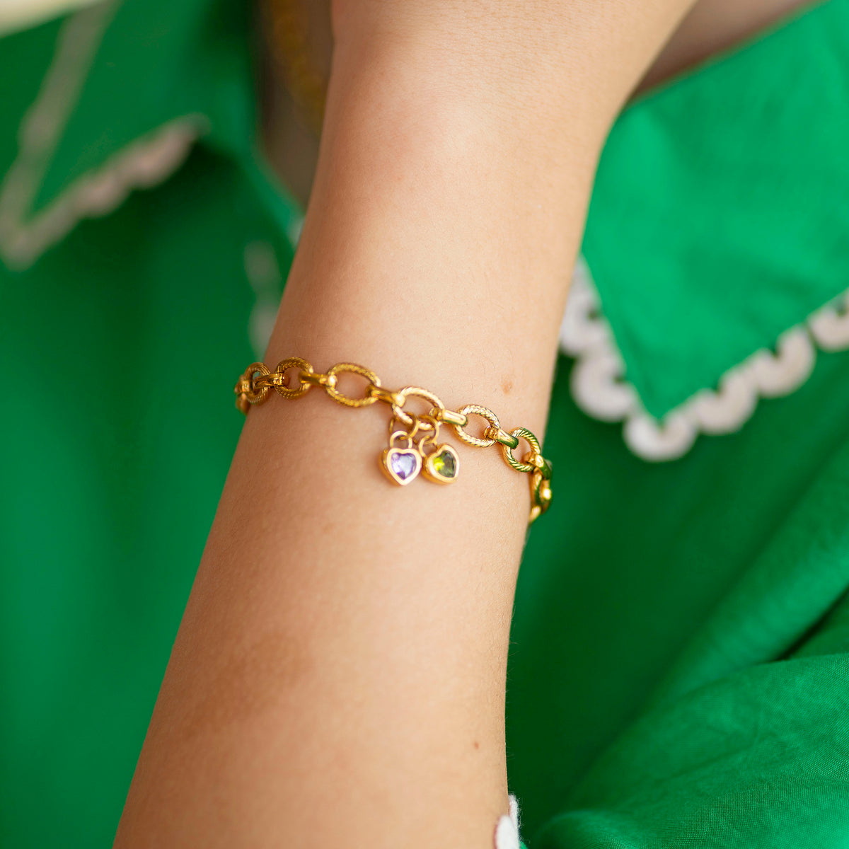 Gold bracelet with heart shaped birthstone charms on a wrist against a green background