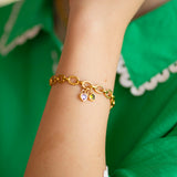 Gold bracelet with heart shaped birthstone charms on a wrist against a green background
