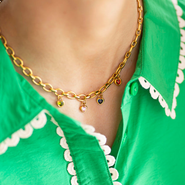 Gold chain necklace with colourful birthstone heart charms worn by a person in a green outfit.