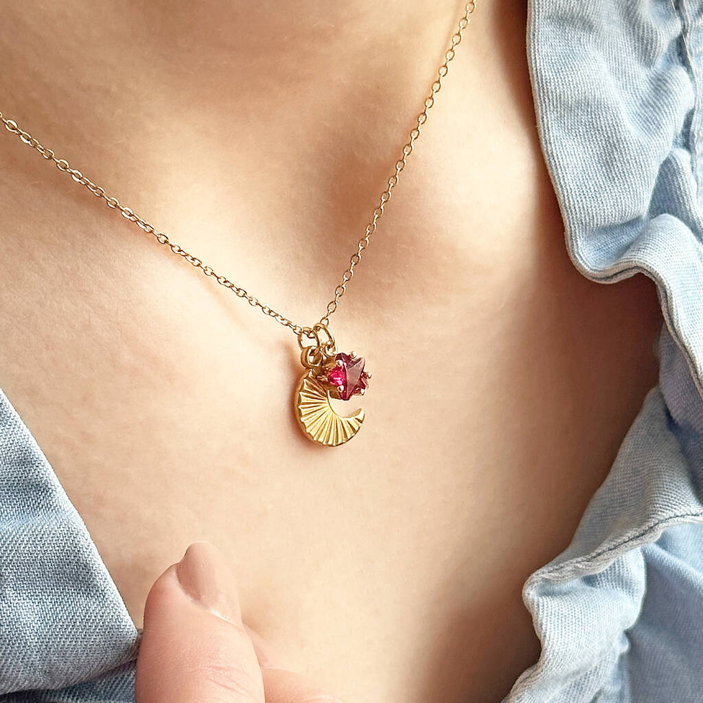 image shows a woman in a denim top wearing a gold moon necklace with birthstone charm detail