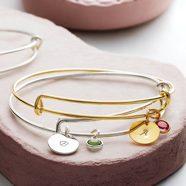 image shows two bangles personalised with hand stamped initial charms and birthstone charms