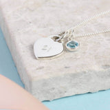 Image shows sterling silver heart charm necklace featuring a '21' engraved heart and March aquamarine Swarovski crystal birthstone. Necklace i on a grey backdrop.
