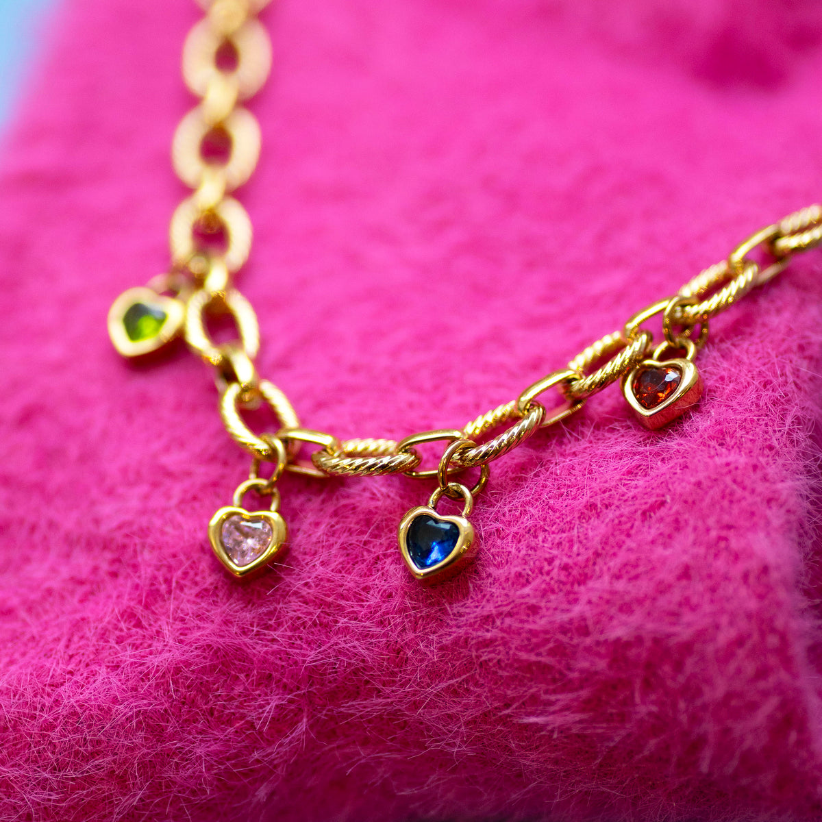 Gold chain necklace with heart shaped birthstone charms on a pink textured background