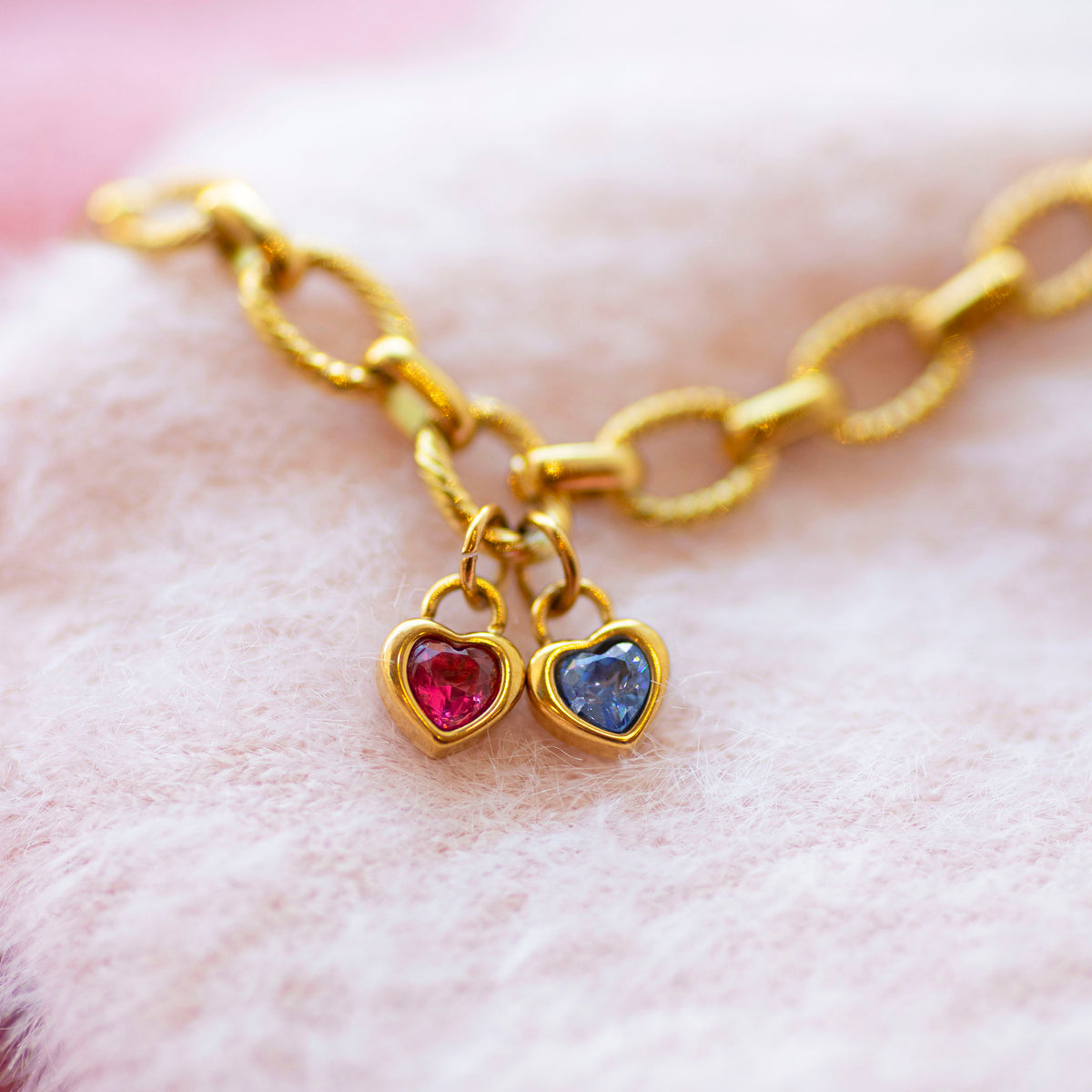 Chunky gold bracelet with heart shaped birthstone charms on a soft pink background