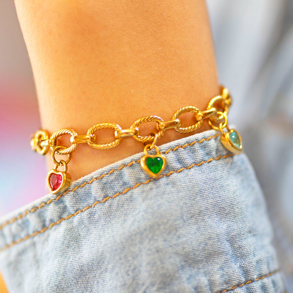 Chunky gold chain bracelet with heart-shaped charms worn on a wrist against a blurred background