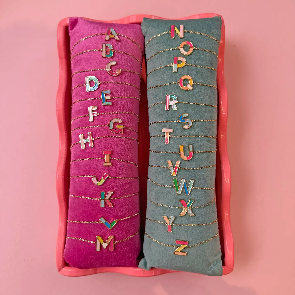 Personalised colourful enamel initial bracelets A to Z with gold plated letter charms displayed on velvet cushions