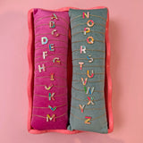 Personalised colourful enamel initial bracelets A to Z with gold plated letter charms displayed on velvet cushions