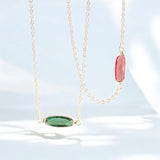 image shows two oblong birthstone necklace against a pale blue background