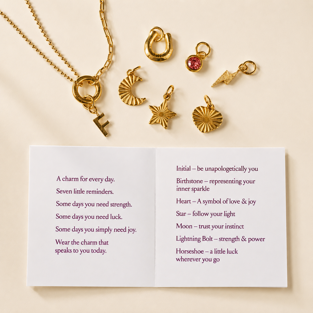 Personalised Week Of Charms Necklace in gold with pink birthstone and star charms styled on a pink heart dish beside interchangeable charms and meaning card.