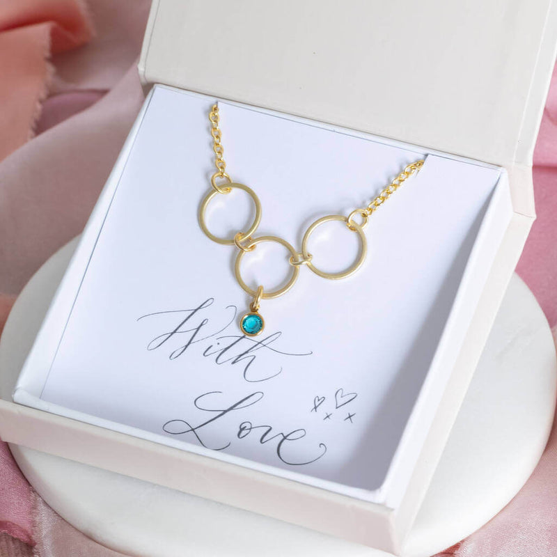 Image shows 30th birthday circles birthstone necklace in a gift box with blue zircon birthstone