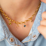 Chunky gold chain necklace with heart shaped birthstone charms worn by a person in a denim shirt.