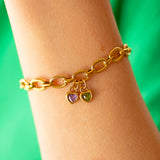 Gold textured chain bracelet with heart shaped birthstone charms on a wrist against a green background
