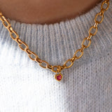 Gold chain necklace with a heart shaped pink gemstone charm on a light grey sweater.