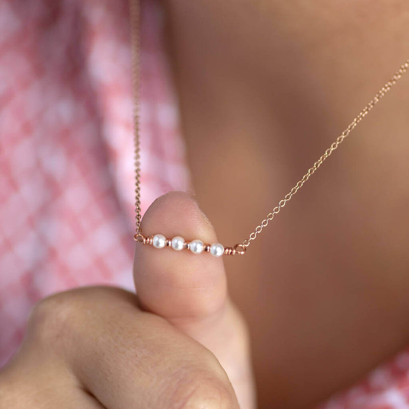 Image shows model pushing out rose gold 40th birthday dainty pearl bar necklace with her thumb