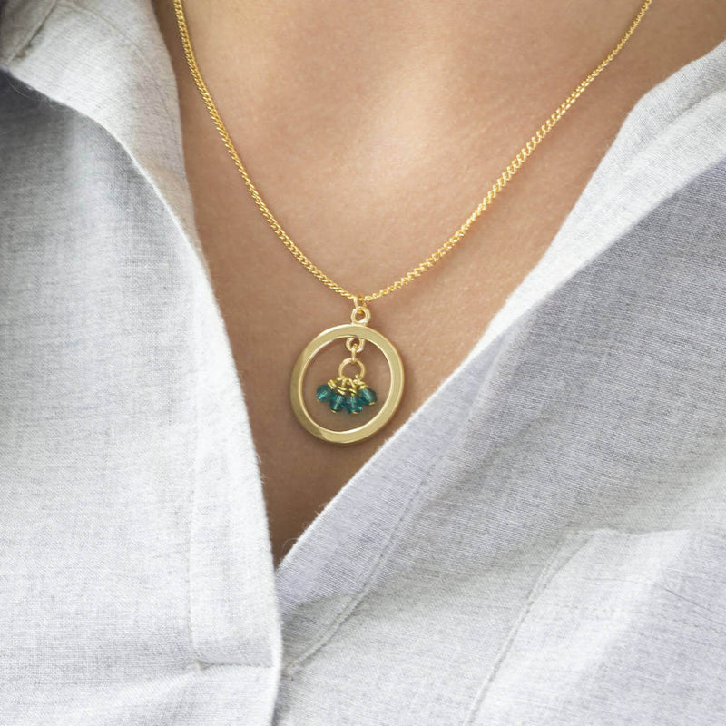 Image shows model wearing 40th birthday gold circle birthstone necklace with blue zircon birthstone