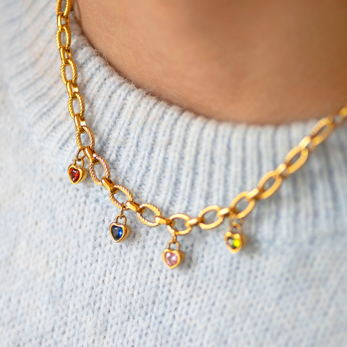 Gold textured chain necklace with heart shaped birthstone charms on a light grey sweater.