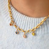 Gold textured chain necklace with heart shaped birthstone charms on a light grey sweater.