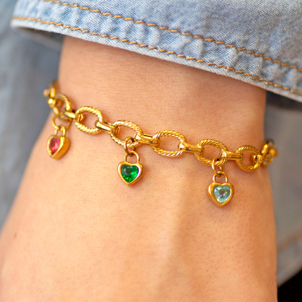 Gold charm bracelet with heart-shaped charms on a person's wrist.