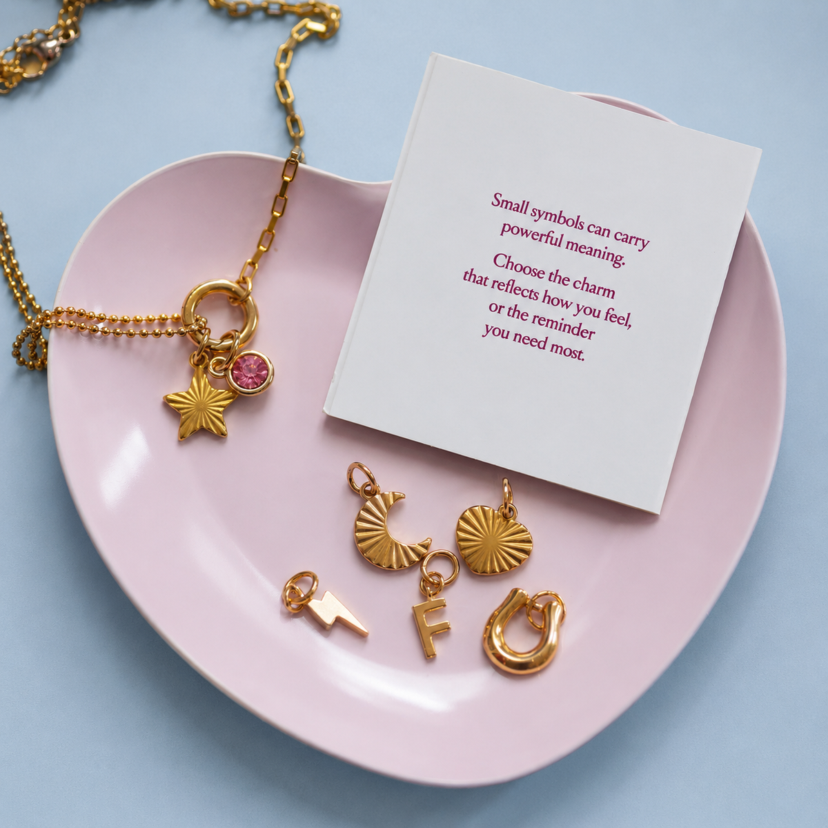 Personalised Week Of Charms Necklace in gold with interchangeable initial, birthstone, moon, star, heart, lightning bolt and horseshoe charms displayed beside meaning card.